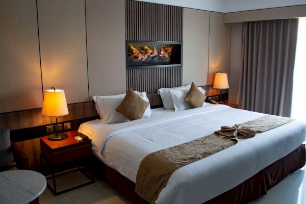 A neatly arranged hotel room with a large bed, two lamps on side tables, decorative pillows, and a wall-mounted art piece above the bed.