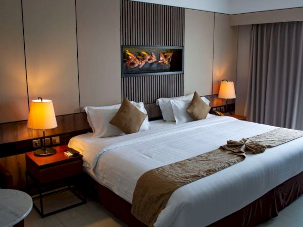 A neatly arranged hotel room with a large bed, two lamps on side tables, decorative pillows, and a wall-mounted art piece above the bed.