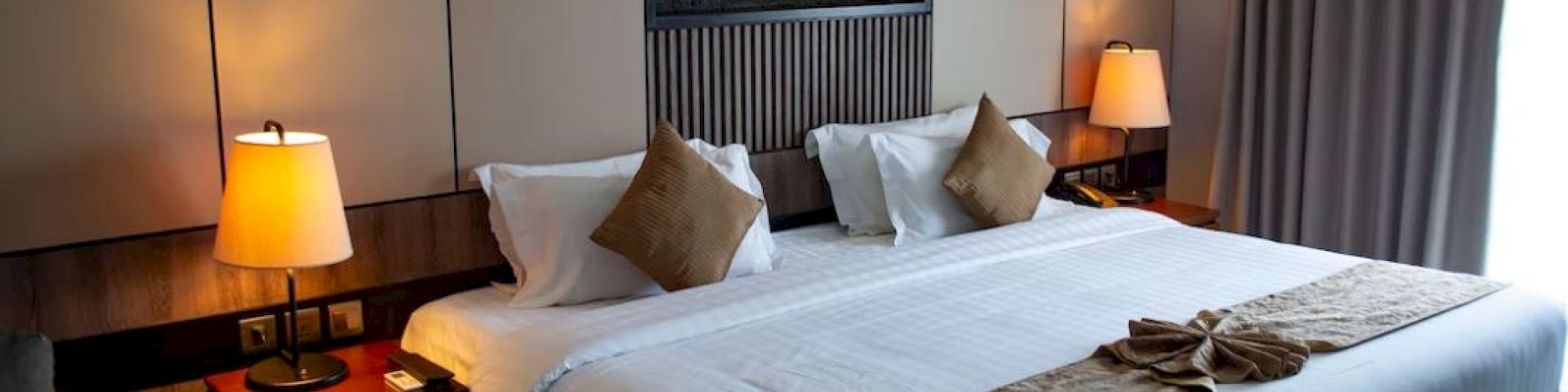 A cozy hotel room with a king-sized bed, decorative pillows, bedside lamps, and elegant wall art above the bed.