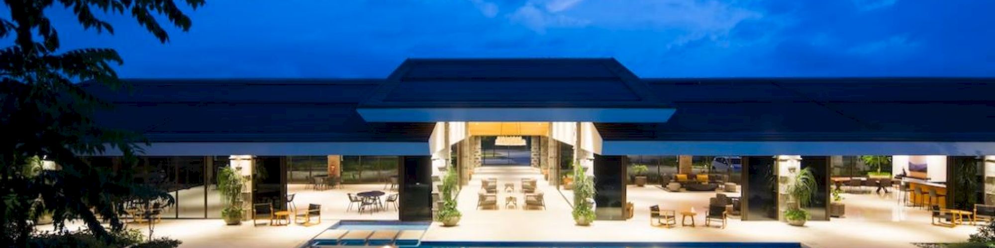 A luxurious outdoor pool area with modern architecture, illuminated at twilight, surrounded by elegant seating and lush greenery.