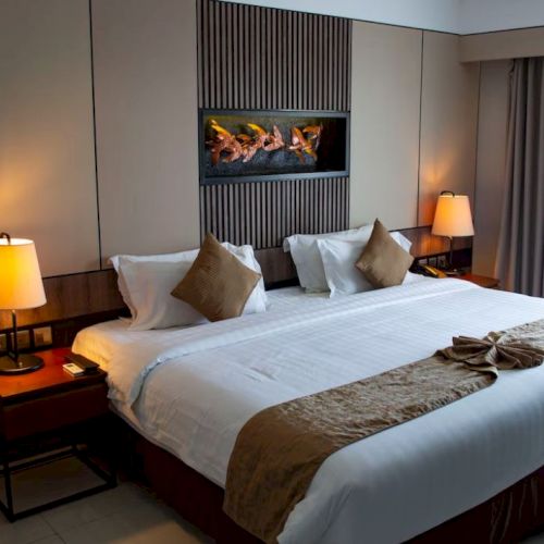 A cozy hotel room with a large bed, decorative pillows, side lamps, and a wall-mounted art piece above the headboard.