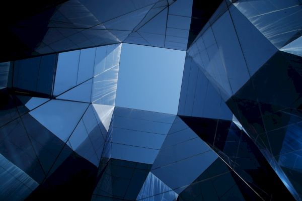 Geometric architecture with a blue sky visible through an opening formed by mirrored, reflective surfaces in an abstract pattern.