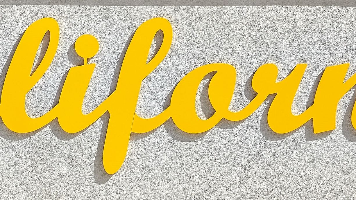 The image shows the word "California" in yellow cursive lettering against a light gray textured background.