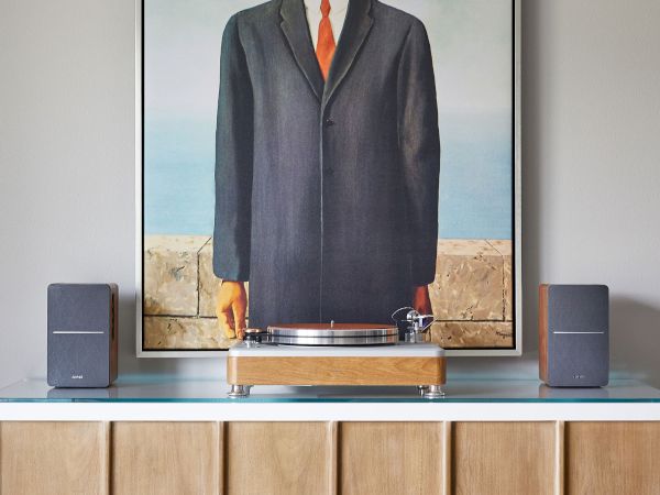 A framed painting of a man with an apple covering his face sits on a cabinet with speakers on either side.