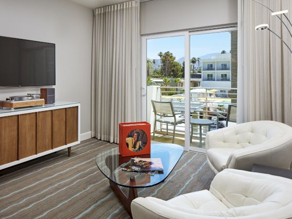 A modern living room with a TV, record player, chairs, coffee table, and balcony view through sliding doors.