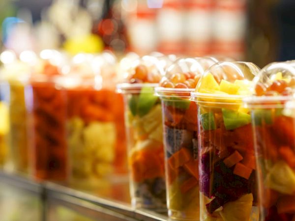 The image shows clear cups filled with assorted fresh fruit pieces, lined up on a counter.
