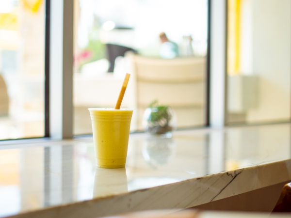A yellow cup with a straw sits on a marble counter near a window, and a small succulent plant is seen in the background.