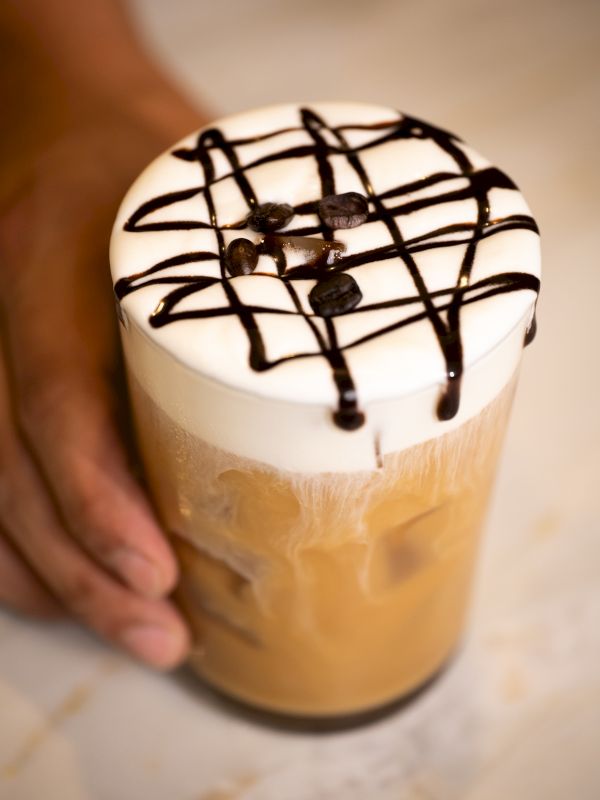 A tall iced coffee drink topped with whipped cream and chocolate drizzle, being held by a hand.