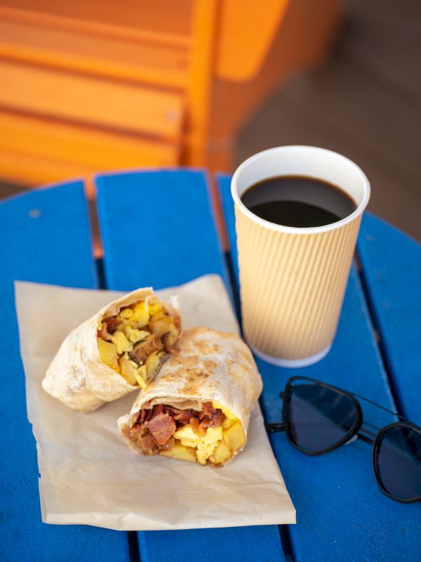 Two pastries on parchment with a cup of coffee and sunglasses on a blue table.