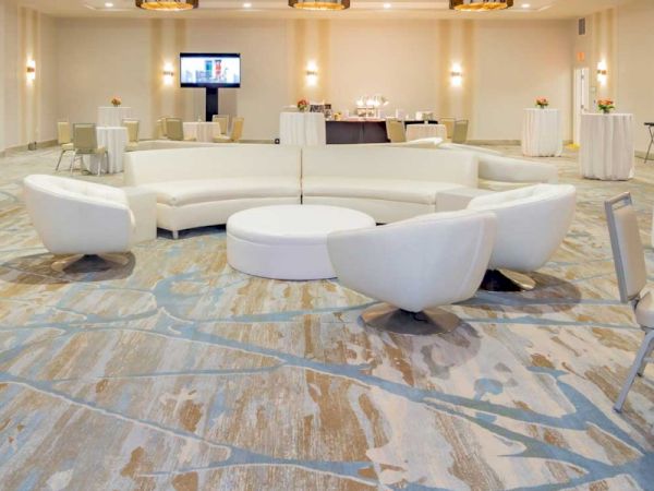 A modern event space with white couches arranged in a circle, patterned carpet, and tables in the background, including a screen.