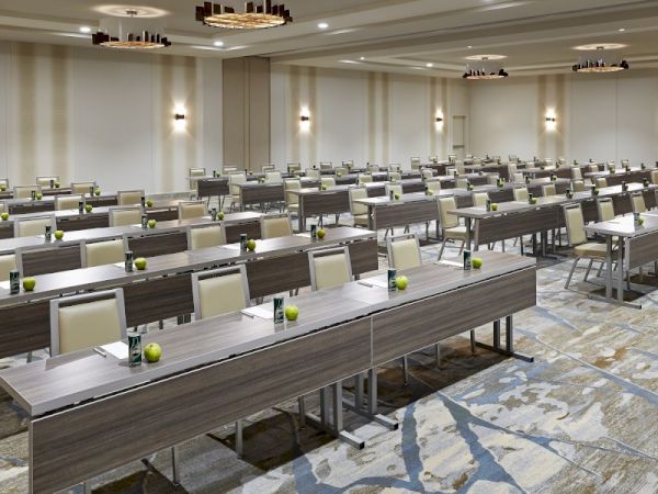 This image shows a conference room with rows of tables and chairs, set up for an event or meeting, with modern lighting fixtures.