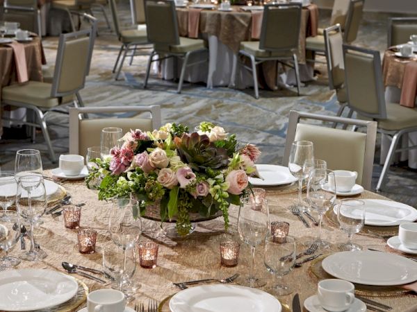 A decorated banquet hall with round tables set for an event, featuring floral centerpieces, glassware, and place settings.