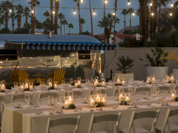 An outdoor dining setup with string lights, candles, and palm trees in the background, creating an elegant and cozy ambiance.