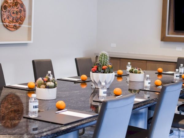 A conference room with a large table set with oranges, water bottles, cacti centerpieces, and chairs. Art decorates the white walls.