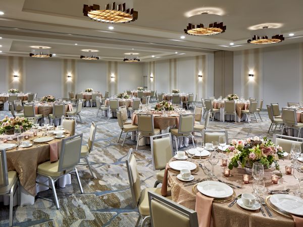 A banquet hall set up for an event, featuring round tables with floral centerpieces, table settings, and modern overhead lighting.