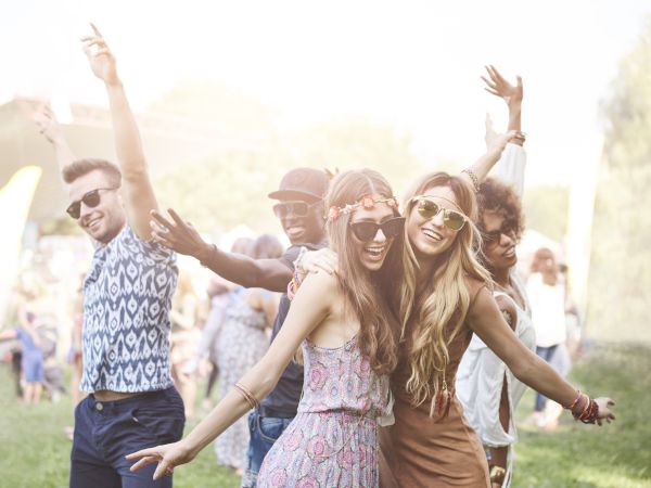 A group of people outdoors, smiling and posing playfully in casual summer attire, suggests they are enjoying a festive, sunny event.