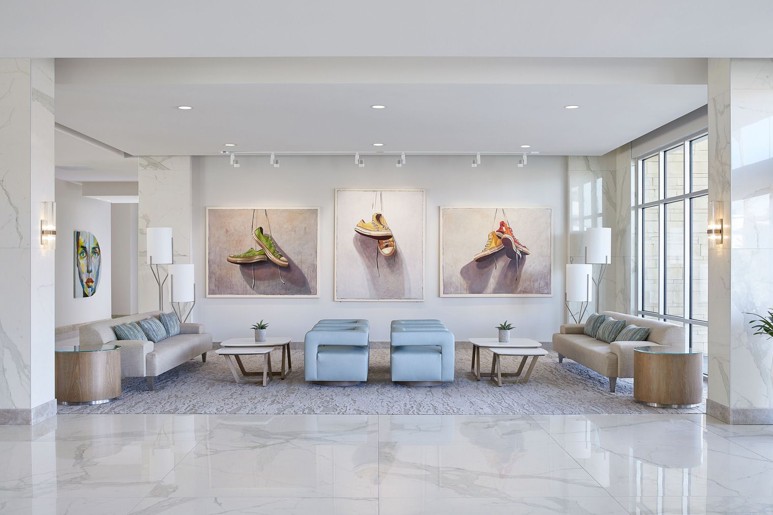 A modern lobby with elegant seating, three large artworks on the wall, soft lighting, and a marble floor creates a serene atmosphere.