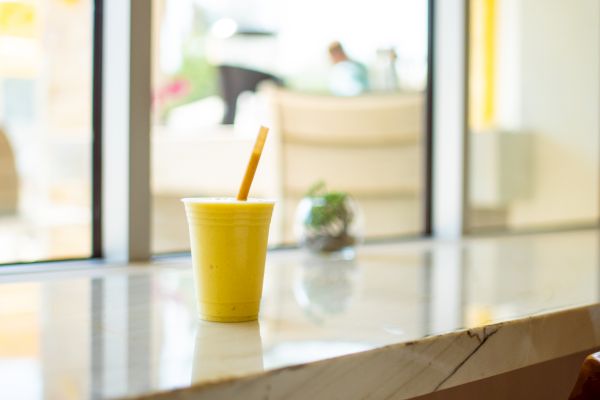 A yellow cup with a straw sits on a marble counter near a window, and a small succulent plant is seen in the background.