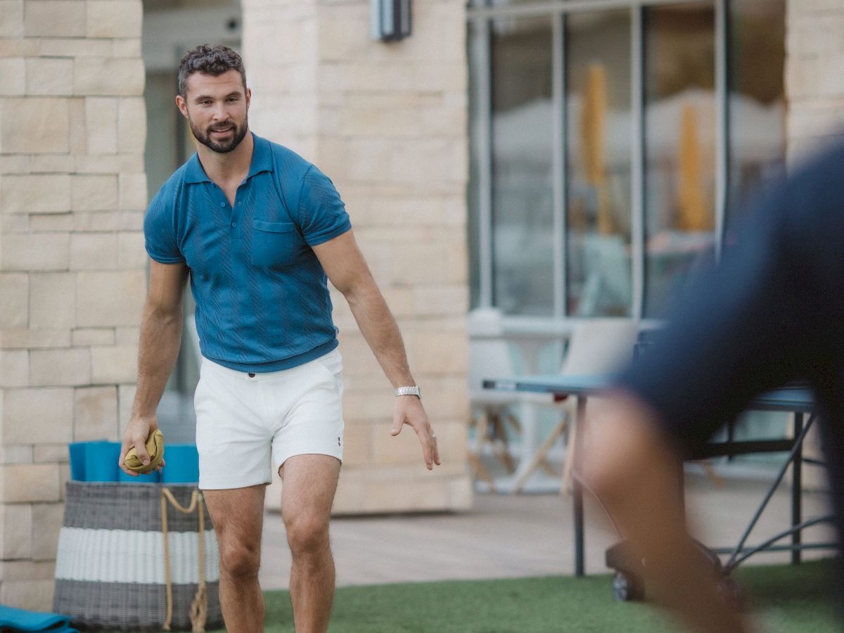 A man is playing cornhole outdoors on a lawn, holding a beanbag, with a cornhole board in front of him.