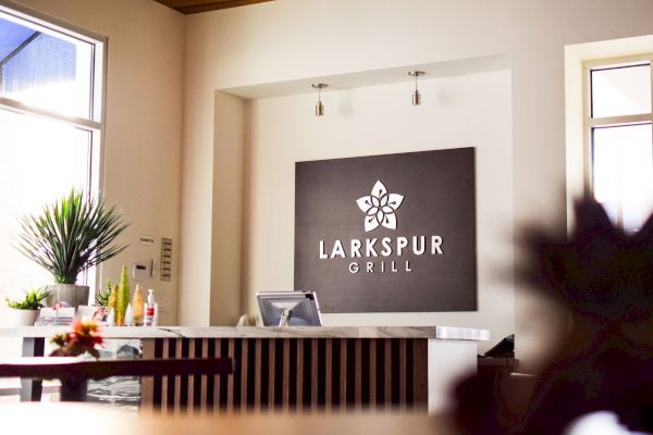 The image shows the reception area of "Larkspur Grill" with a sign, countertop, and plants, creating a welcoming atmosphere.