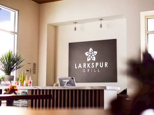 The image shows the reception area of "Larkspur Grill" with a sign, countertop, and plants, creating a welcoming atmosphere.