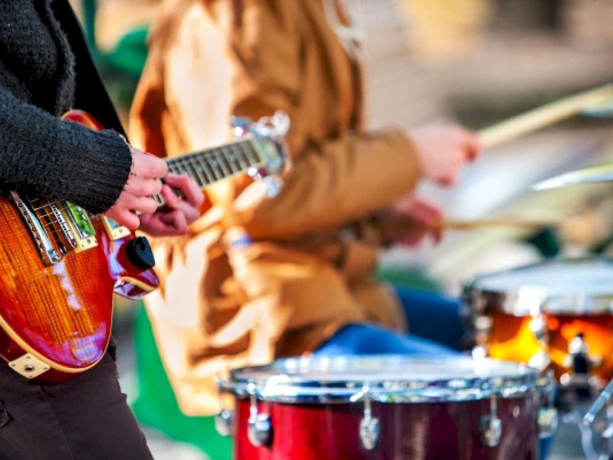 A guitarist and drummer are playing their instruments outdoors, captured in a dynamic performance setting.