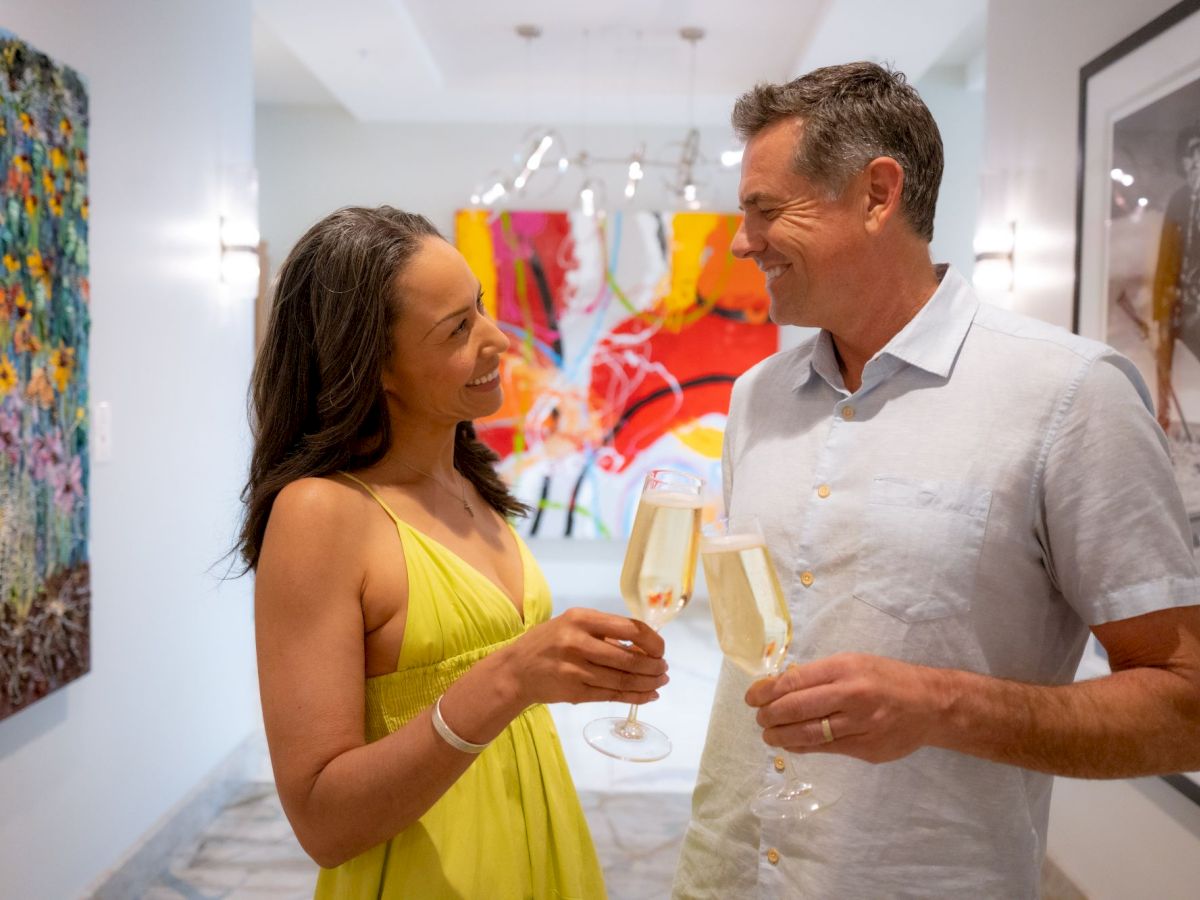 A man and woman chat and toast with champagne flutes in an art gallery.