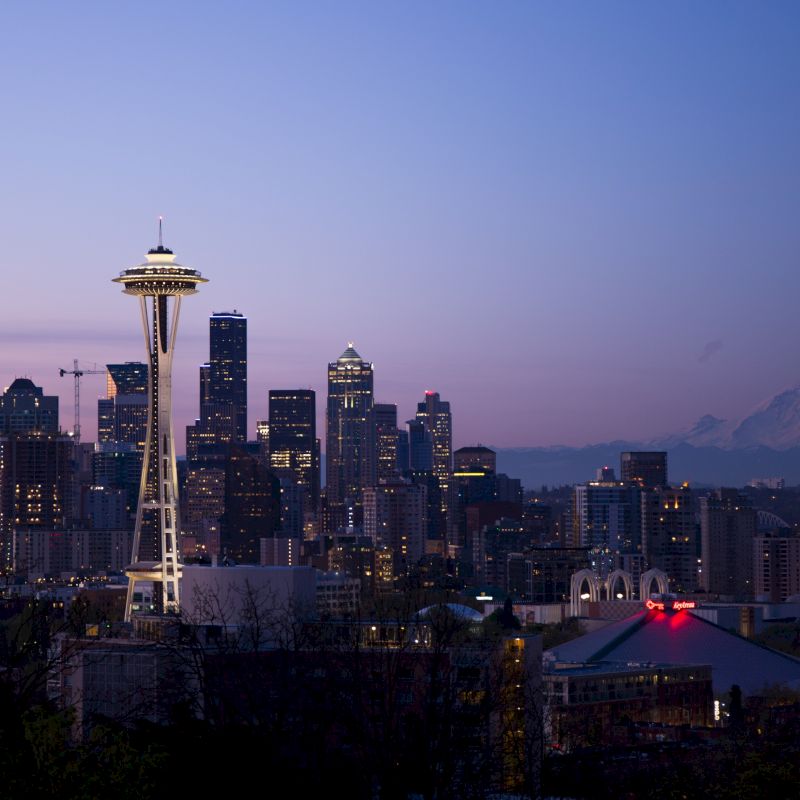 Seattle skyline at dusk with the Space Needle and Mount Rainier in the background, against a clear sky.