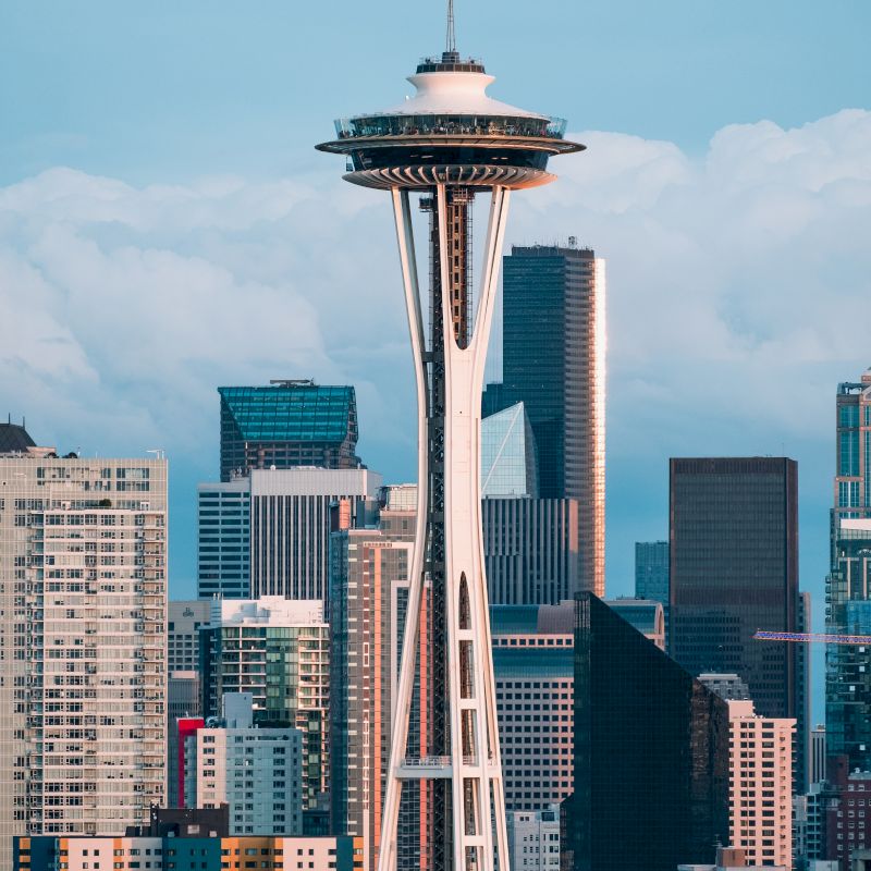 The image shows the Space Needle with surrounding city skyscrapers against a clear sky.