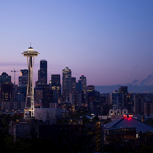 Seattle skyline at dusk with the Space Needle and Mount Rainier in the background against a purple sky.